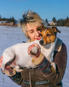 Vertrauen schaffen für die Hund-Mensch-Beziehung. Masha hält lächelnd ihren Jack Russel Terrier im Arm, der schmutzige Pfötchen hat.